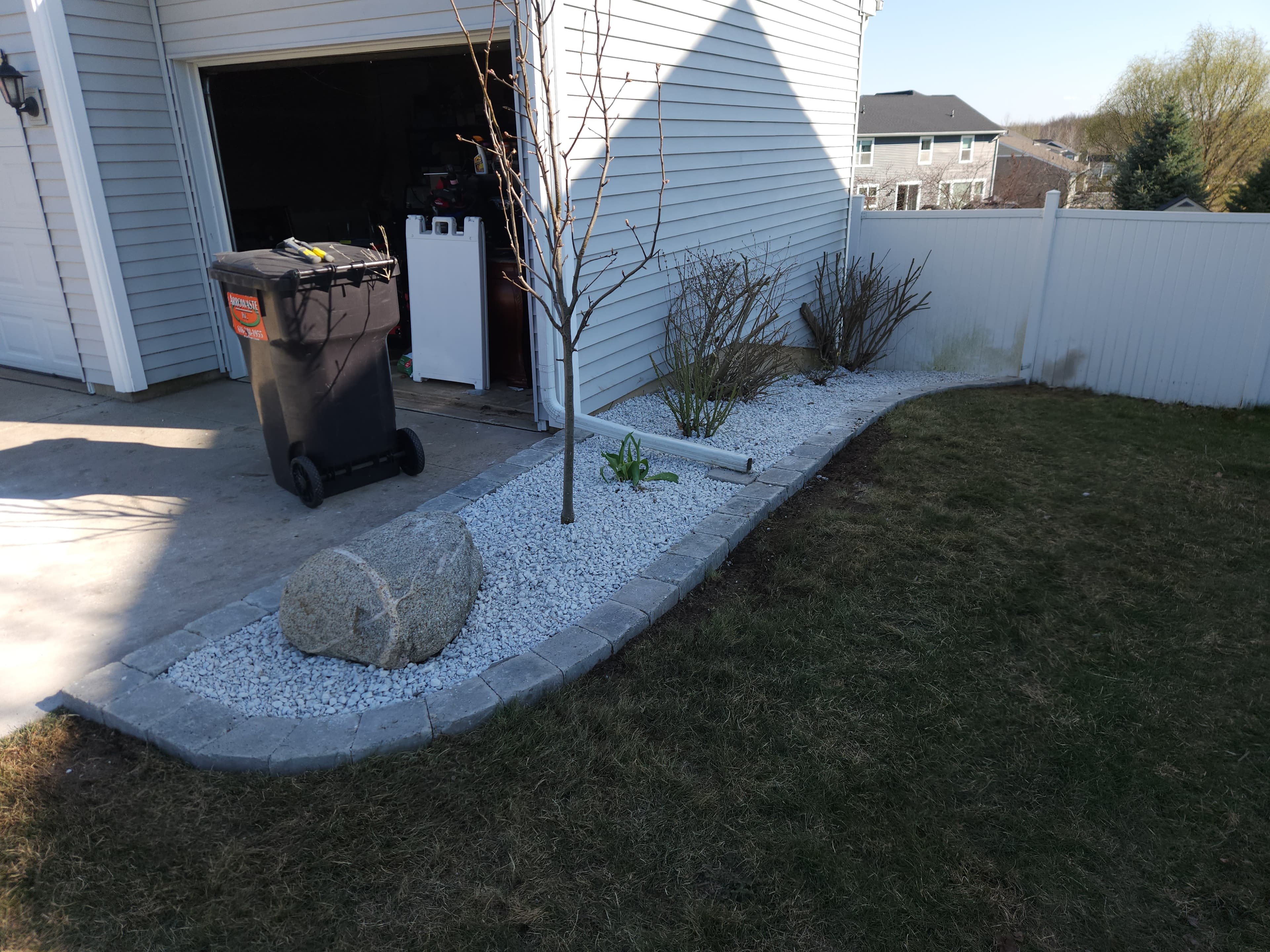 Curved paver-edged landscape bed with white rock, a small tree, and a decorative boulder