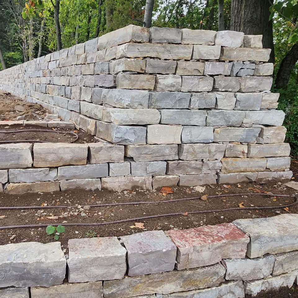 Tall multi-colored block retaining wall with stone steps and river rock on a hillside