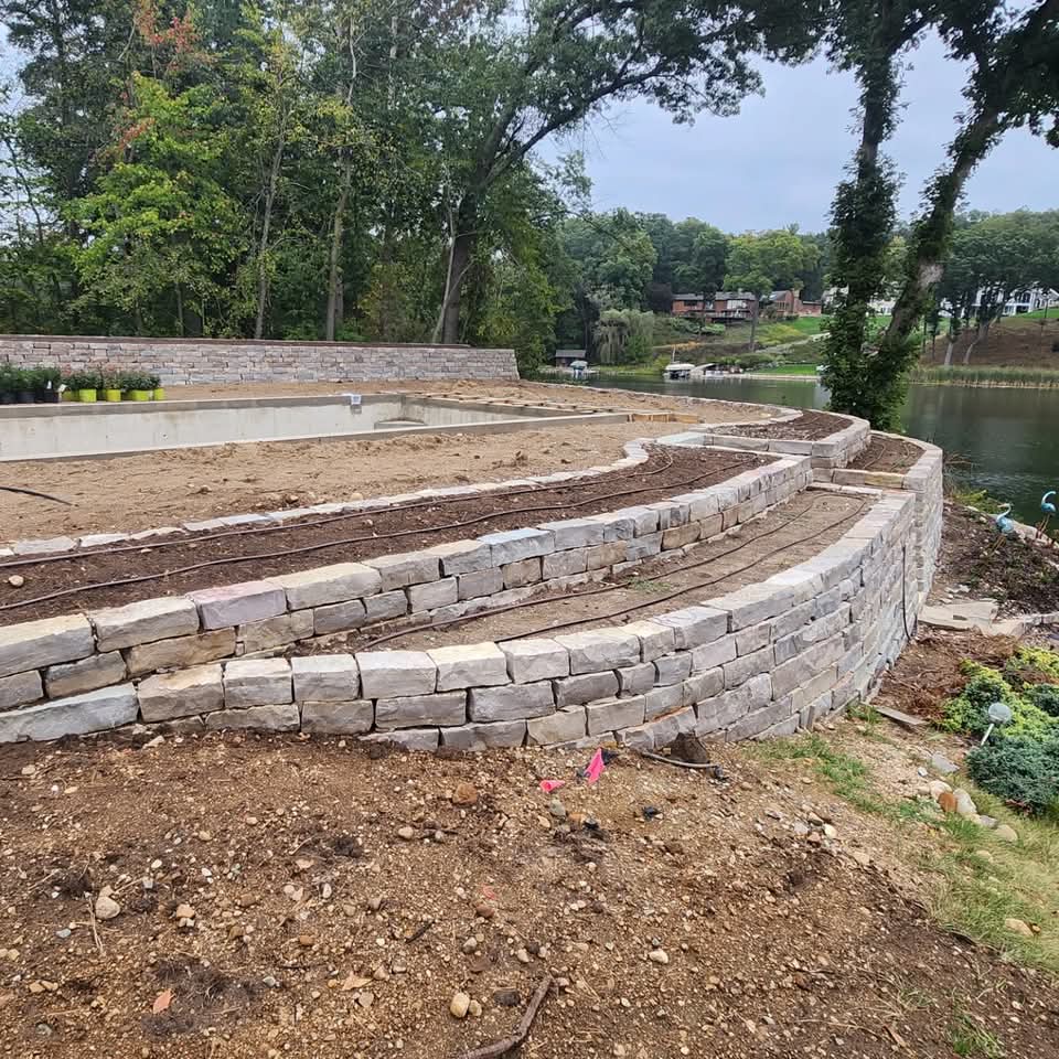 Curved natural stone retaining wall along a lakefront with prepared planting bed on top