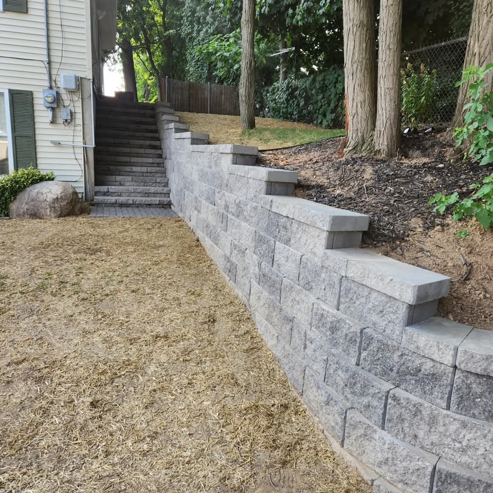 View looking down gray block steps alongside a retaining wall with paver landing visible below