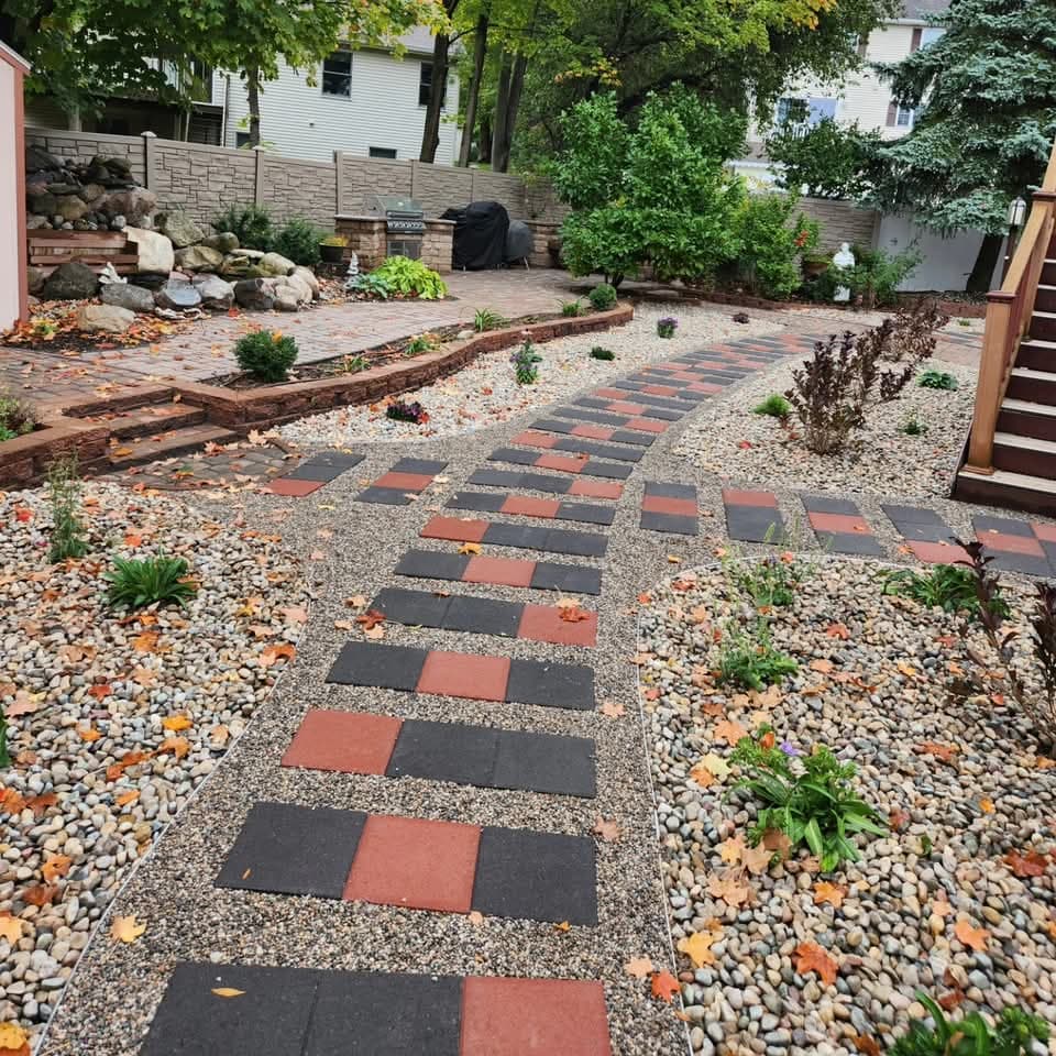 Red and black checkerboard paver walkway flanked by pea gravel beds scattered with autumn leaves