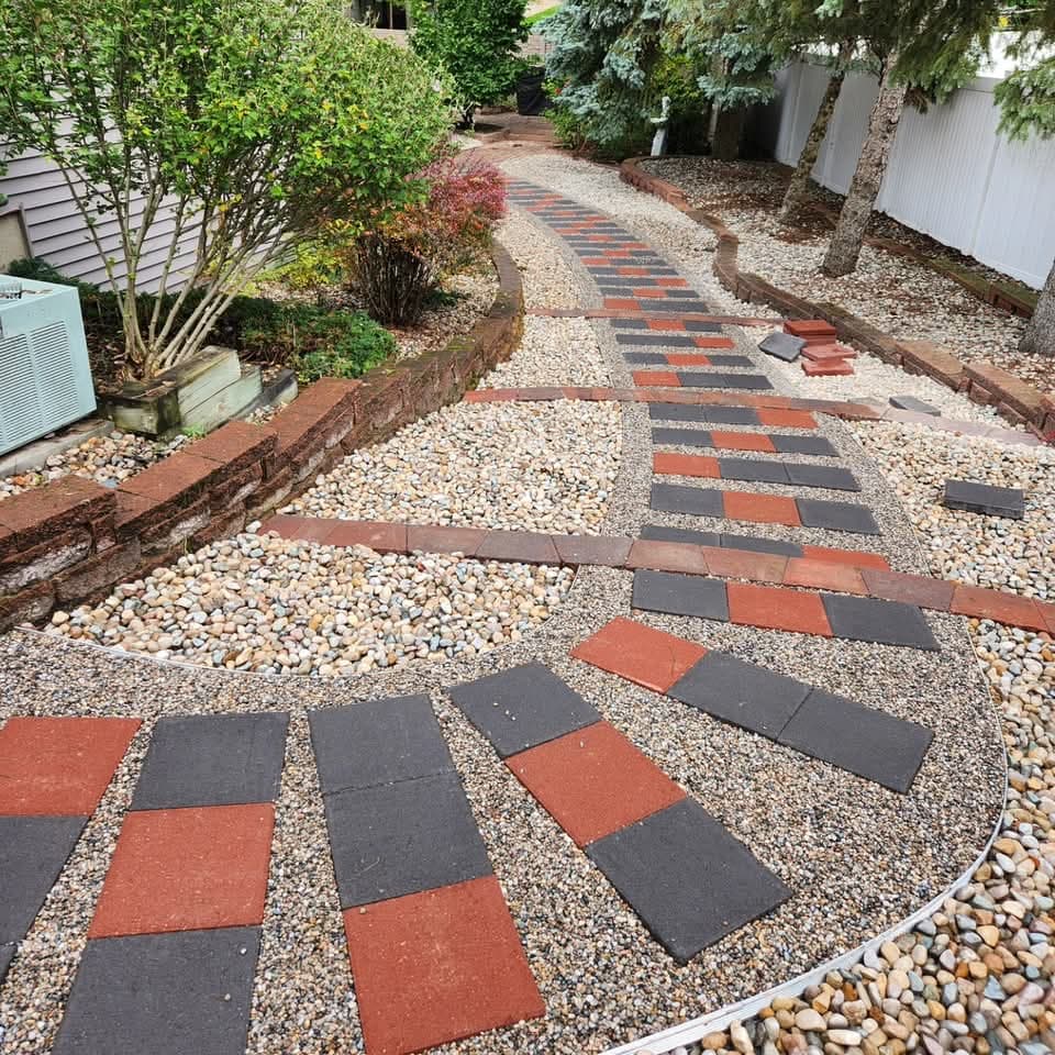 Curving walkway of red and black paver squares set in pea gravel through a landscape bed