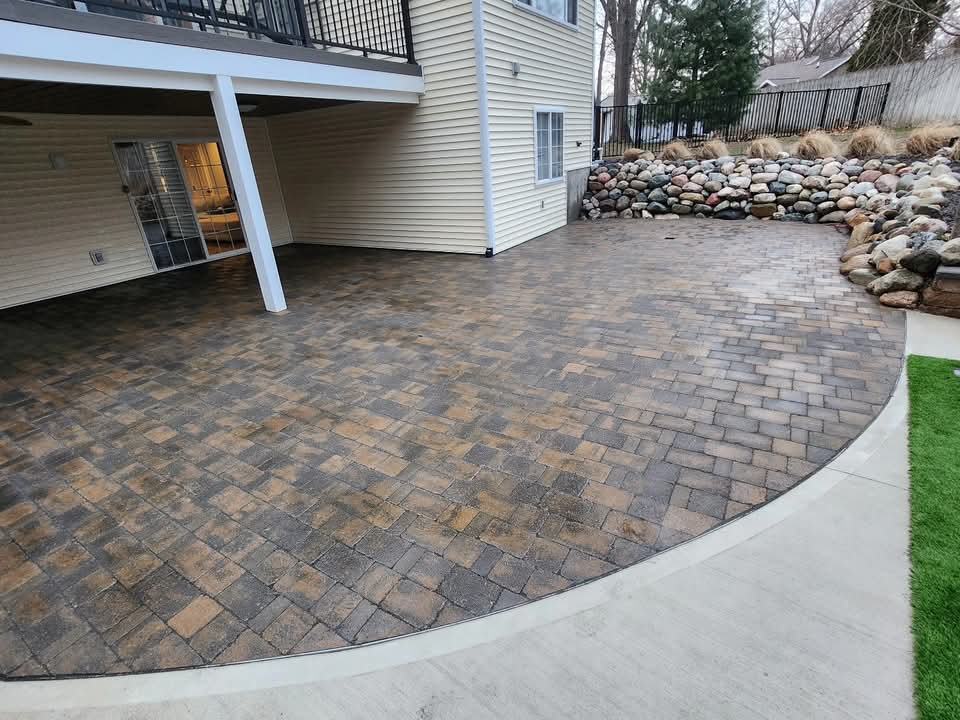 Gray block retaining wall with integrated block steps and fresh topsoil behind it, running between two houses in a residential backyard, a basketball hoop and dark mulch bed visible at the top of the slope