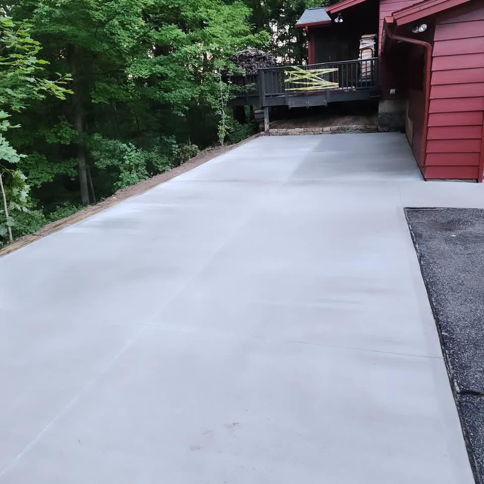 Freshly poured smooth-finished concrete driveway running alongside a red-sided West Michigan home