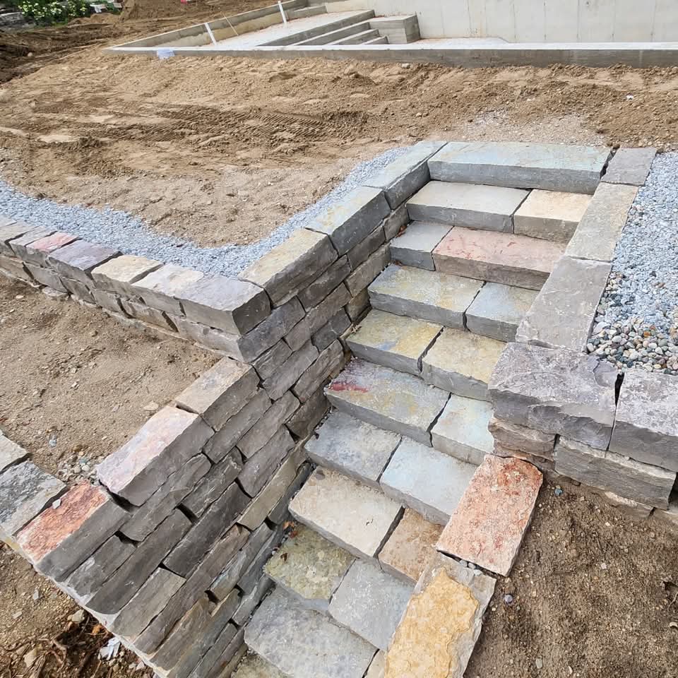 Natural stone steps with retaining wall curving at a landing with crushed stone base and graded hillside behind