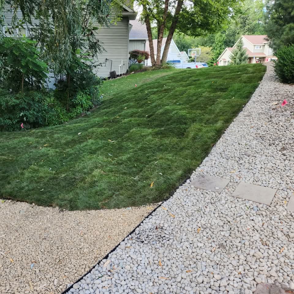 Newly laid green sod lawn bordered by a white river-rock drainage strip beside a home