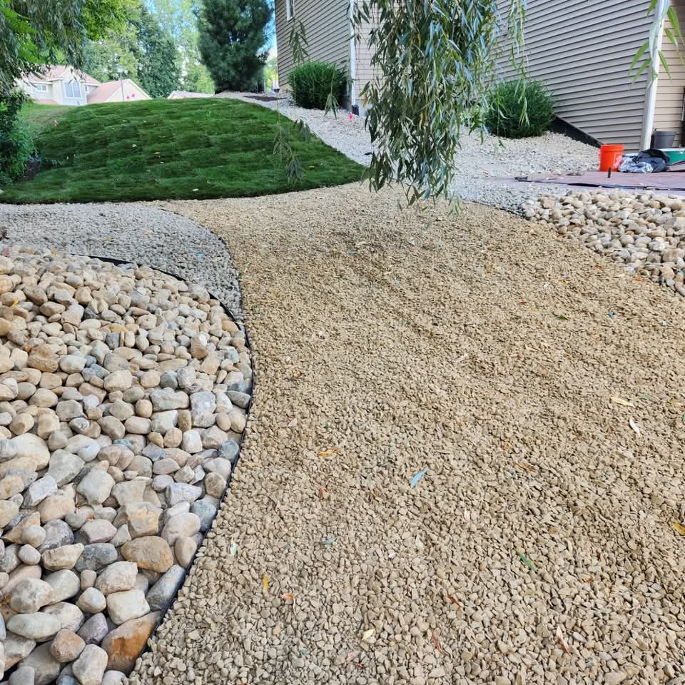 Pea gravel drainage strip framed by river rock alongside a freshly sodded lawn