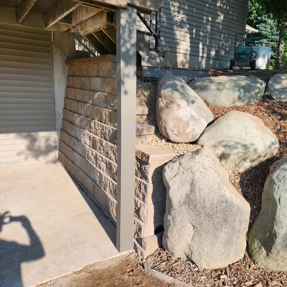 Block retaining wall under a raised deck with large boulders and wood chip mulch transitioning to the adjacent yard