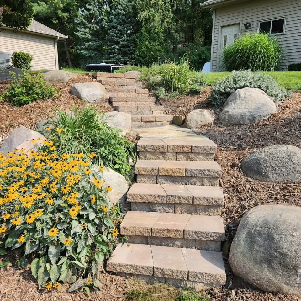 Paver staircase climbing a mulched landscape bed with boulders and bright black-eyed Susan flowers