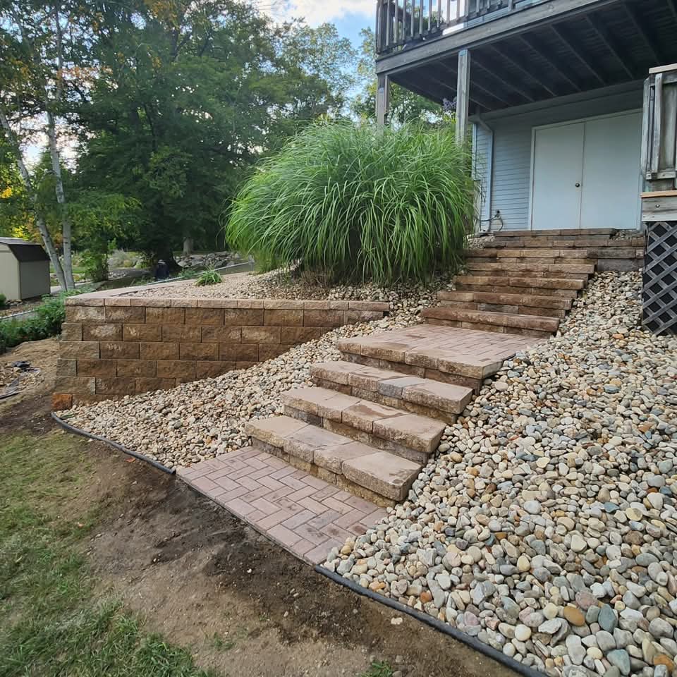 Brown paver stairway flanked by river rock beds beside a backyard deck