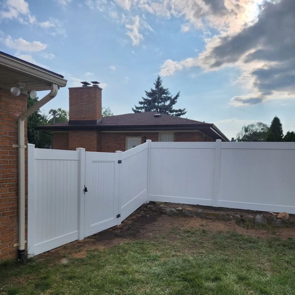 Backyard of a red brick ranch house with a new circle-pattern paver patio, stone step landing at the sliding glass door, and white vinyl privacy fence behind