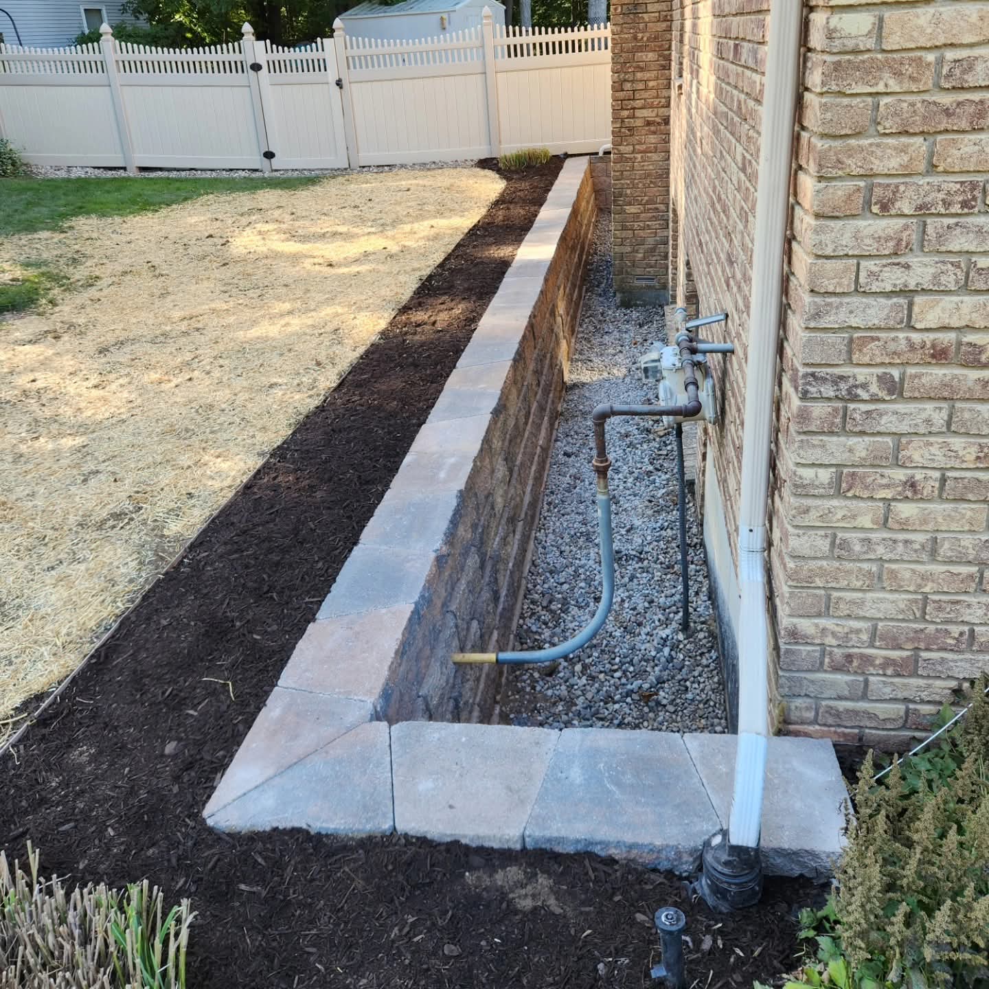 Narrow side-yard retaining wall and raised mulched bed beside a brick West Michigan home