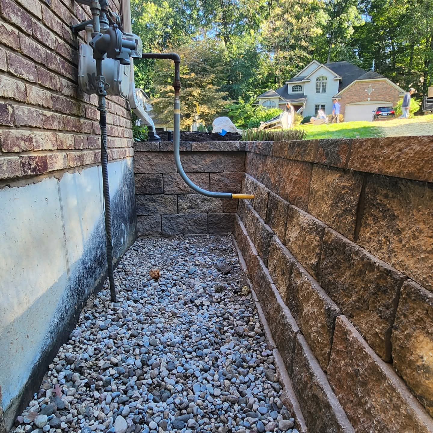 Tan block retaining wall with a gravel drainage channel along the side of a brick home