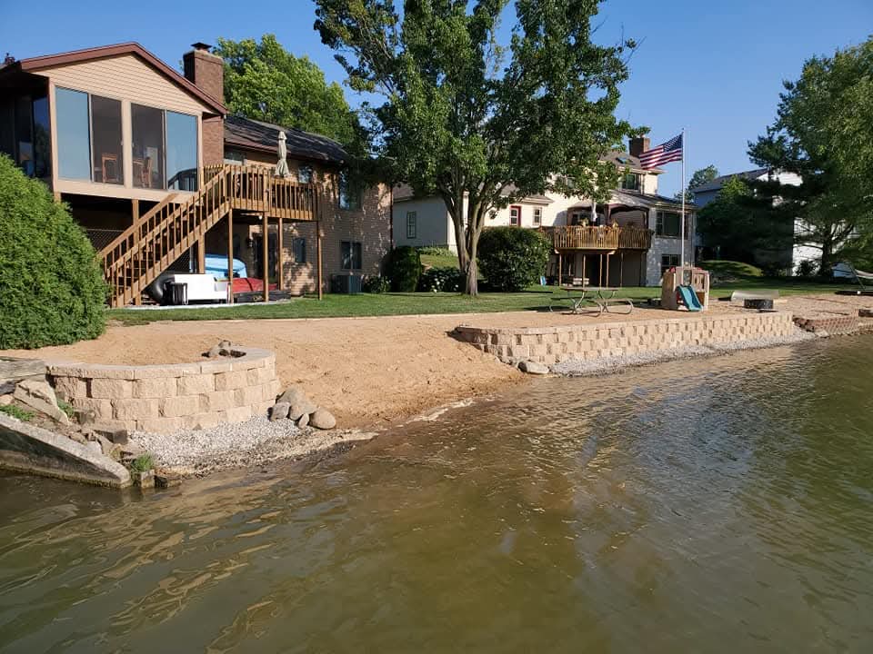 Lakefront property with a curved tan block retaining wall and sand beach in front of a home