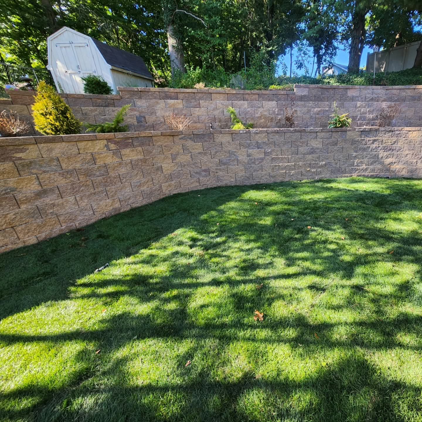 Tan tiered block retaining wall with planter terraces behind a shaded green lawn