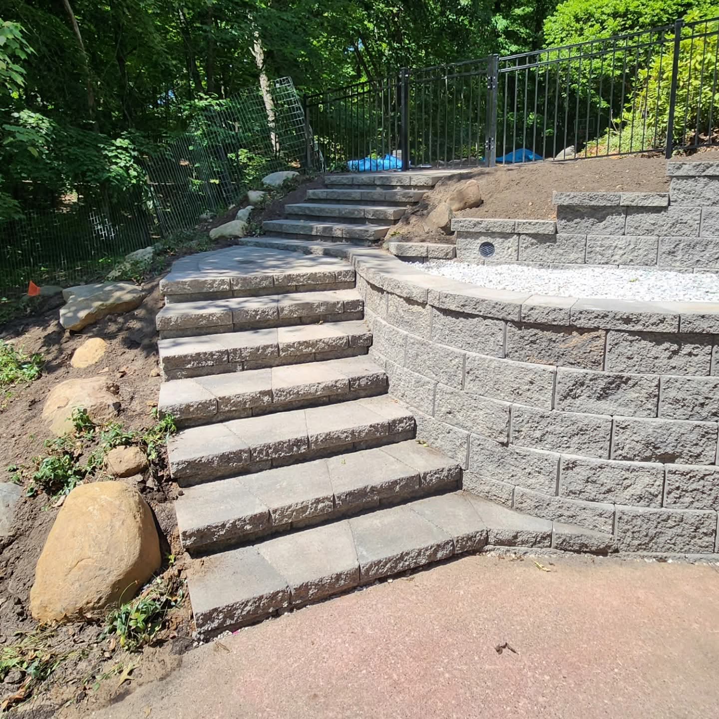 Long gray block staircase climbing alongside a curved retaining wall with wrought-iron railing