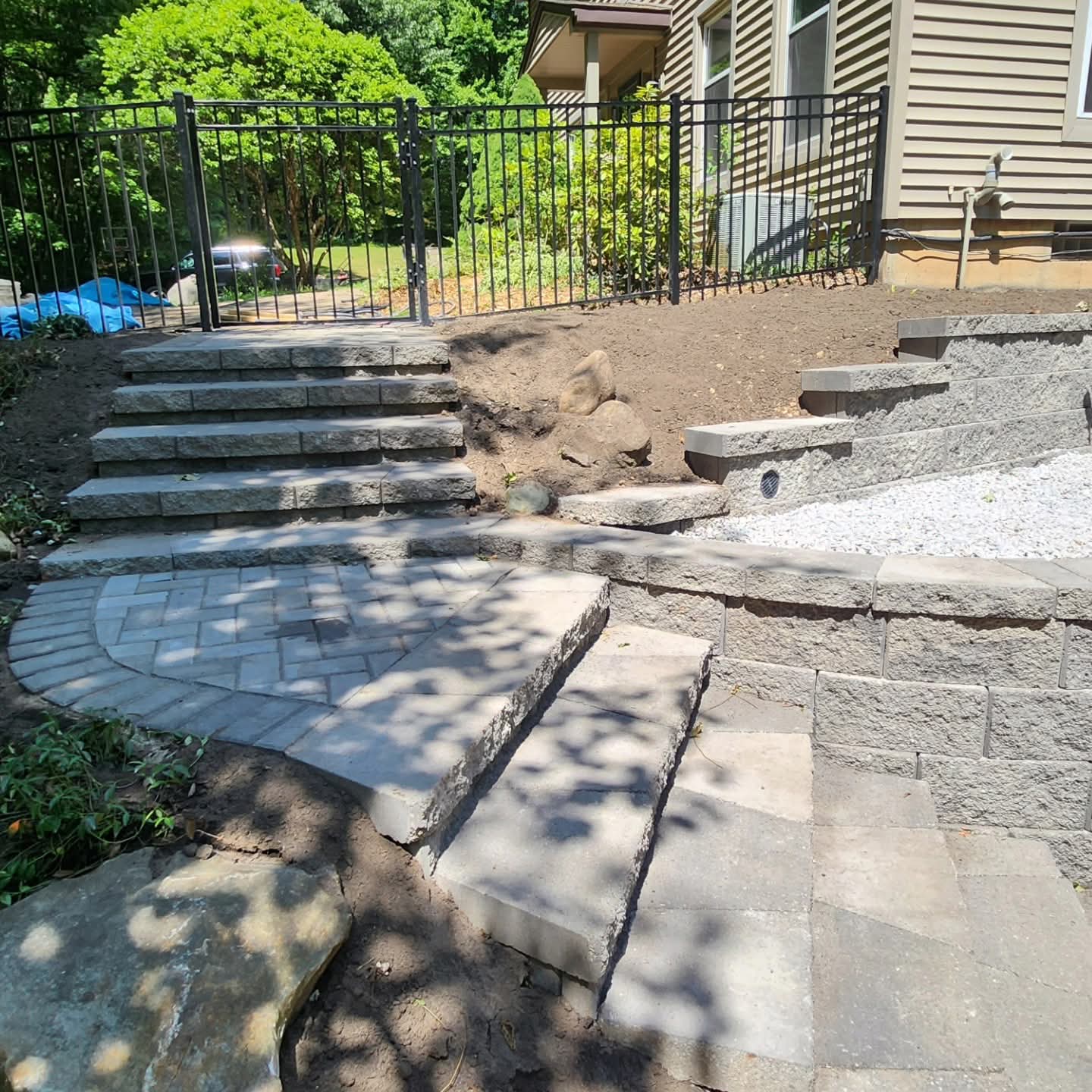 Backyard hardscape combining a gray paver patio, block steps, and a small retaining wall